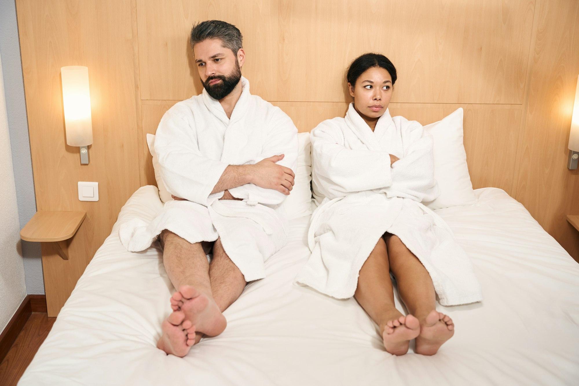 Sad couple in bathrobes sitting in silence in hotel room