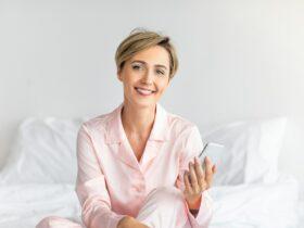 Happy woman sitting in bed using cell phone